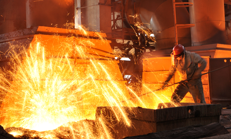 Worker in protective gear next to blast furnace making iron